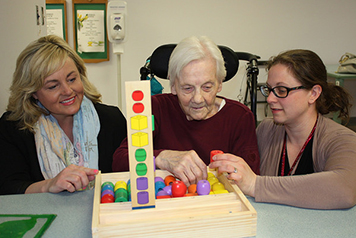 Monica Bretzlaff, BSO Provincial Manager (left), and Nurse Practitioner Shannon Cadieux (right), facilitate a Montessori-based dementia activity with Gert.